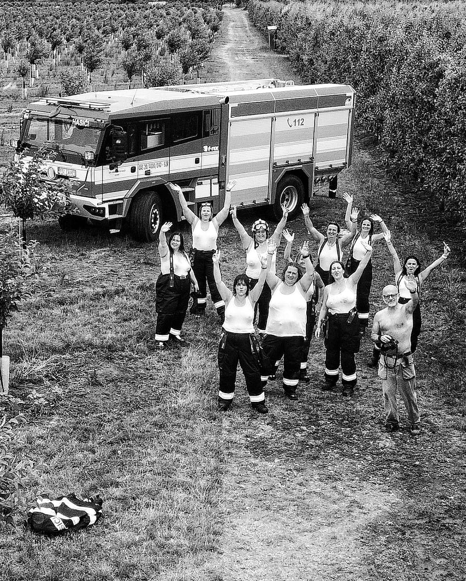 Pohled shora na skupinu hasiček se zdviženýma rukama před cisternou