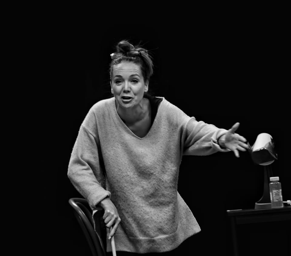 A black and white frame of an actress on stage mid-gesture, the background falling to black