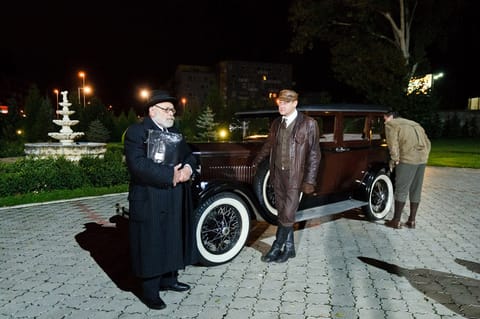 Noční scéna u historického automobilu, tři muži v dobových kostýmech