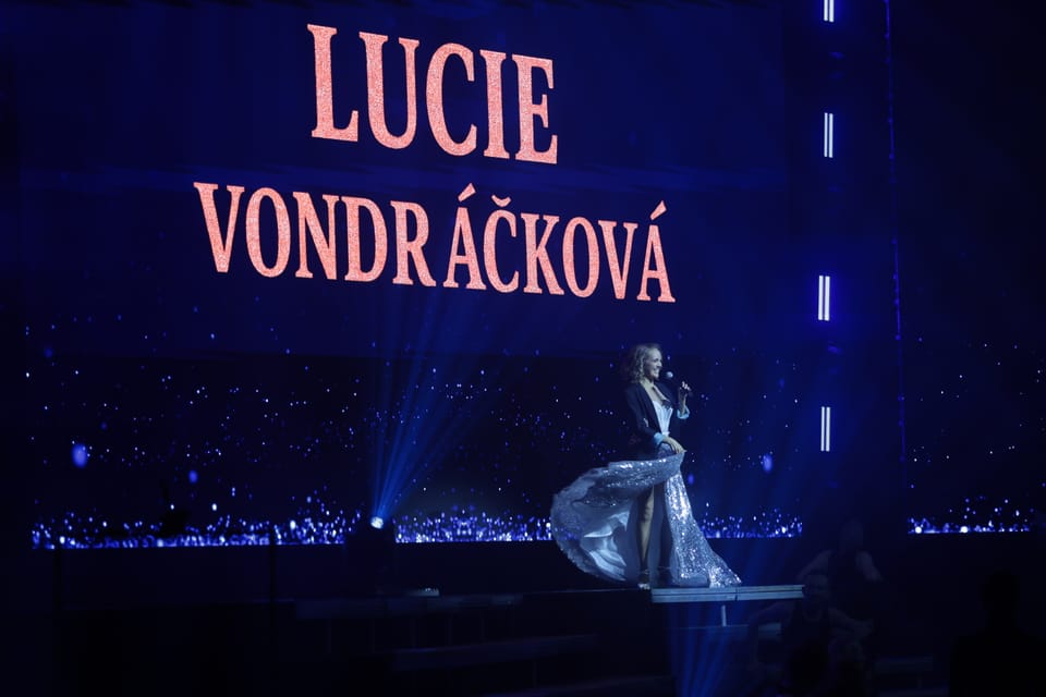 A concert stage, the performer's name lit above a figure in a long gown