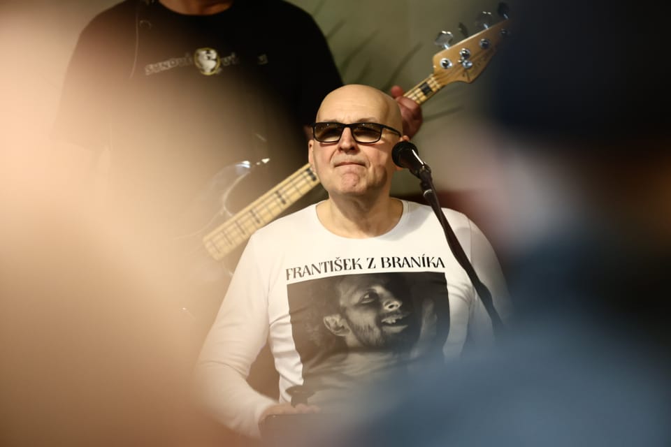A singer in dark glasses at the microphone, the band behind him
