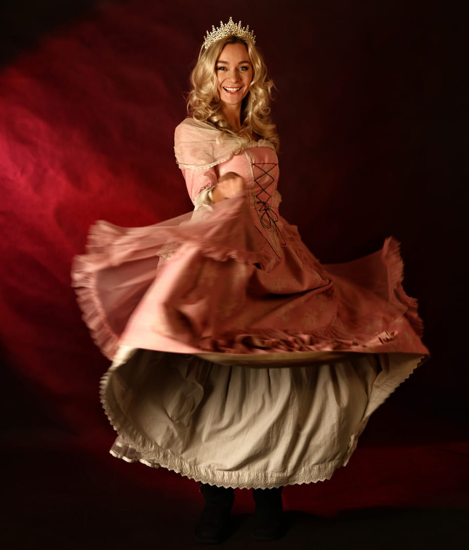 An actress in a coronet spinning the skirt of a period dress against red