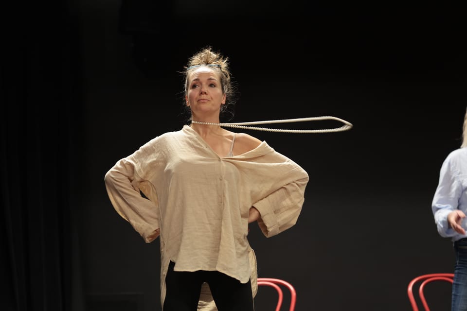 An actress spinning a loop of rope above her head on the dark stage