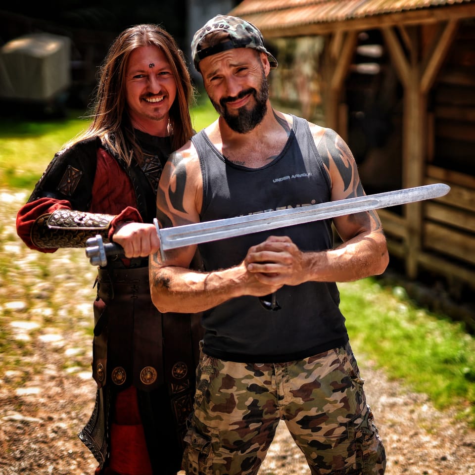 Two men holding a long sword together, one of them in period costume