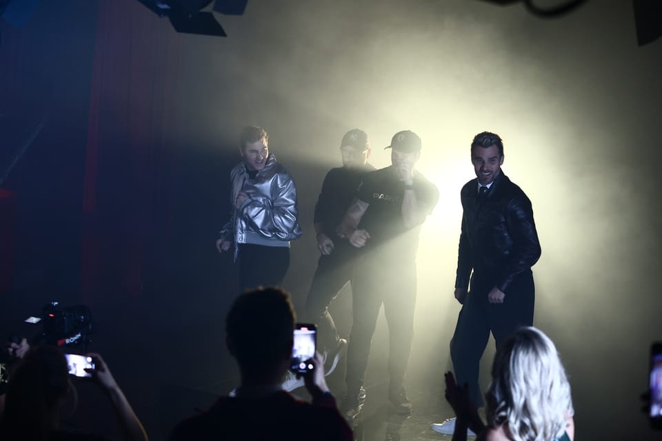 Figures in stage haze against the spotlights, the audience filming in the foreground