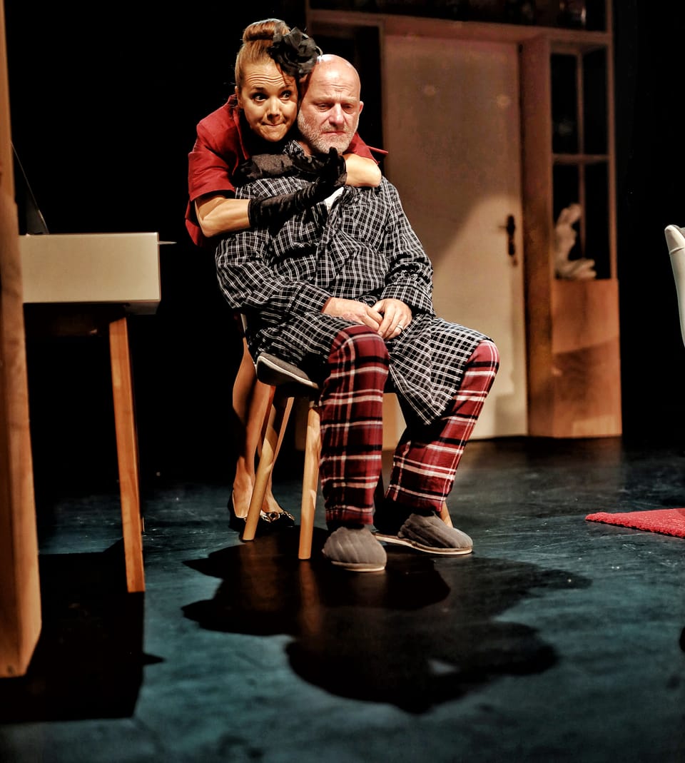 An actress sitting on a man's lap centre stage, he in checked trousers