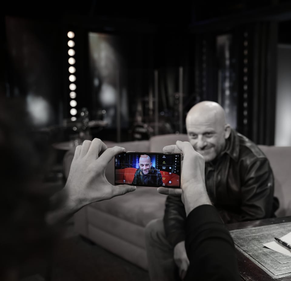 Hands holding a phone, filming a man in the dressing room under a row of bulbs