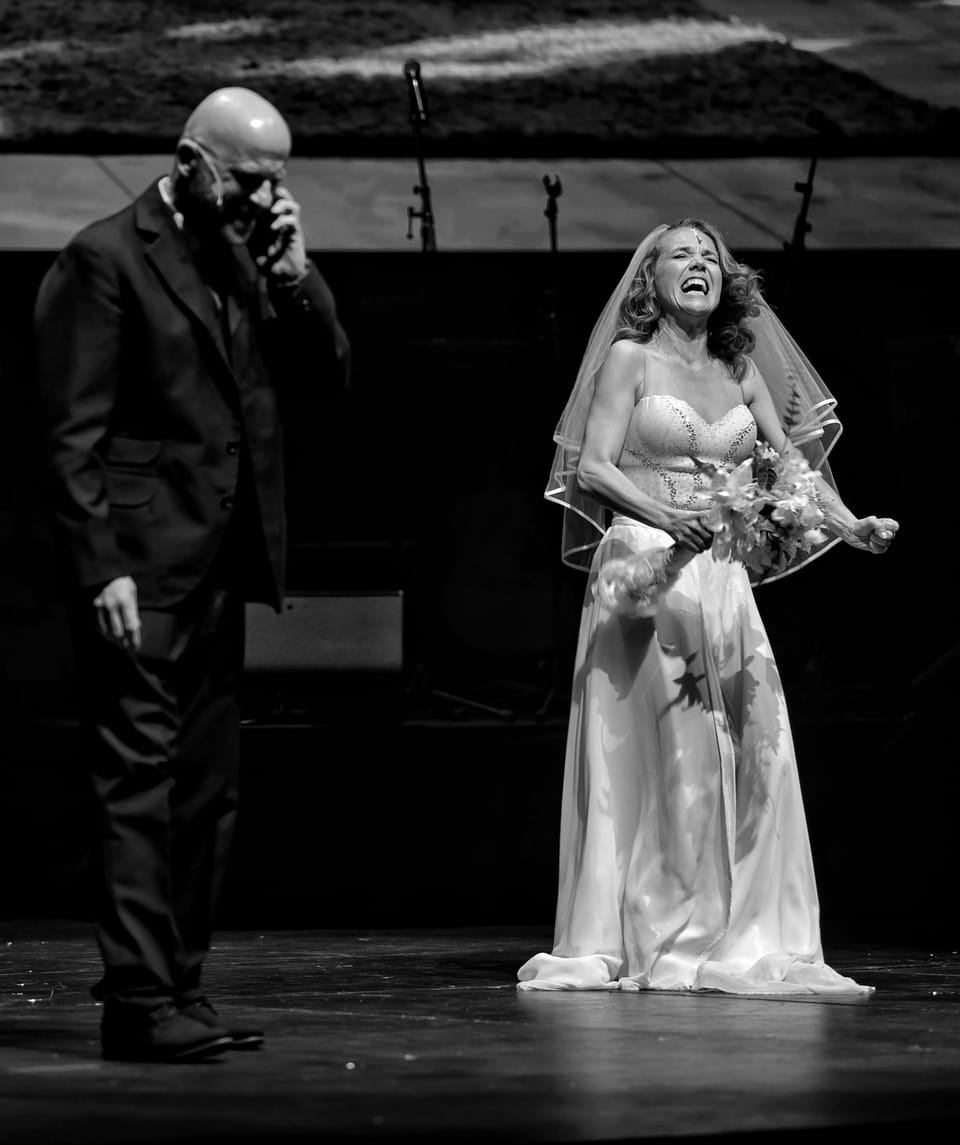 A bride with a bouquet centre stage, the man beside her covering his face