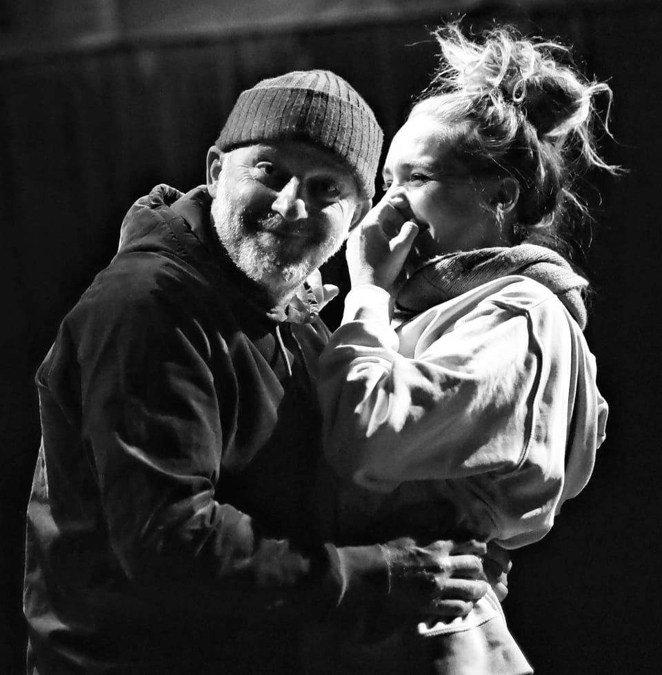 A couple in hoodies embracing, both laughing into the lens