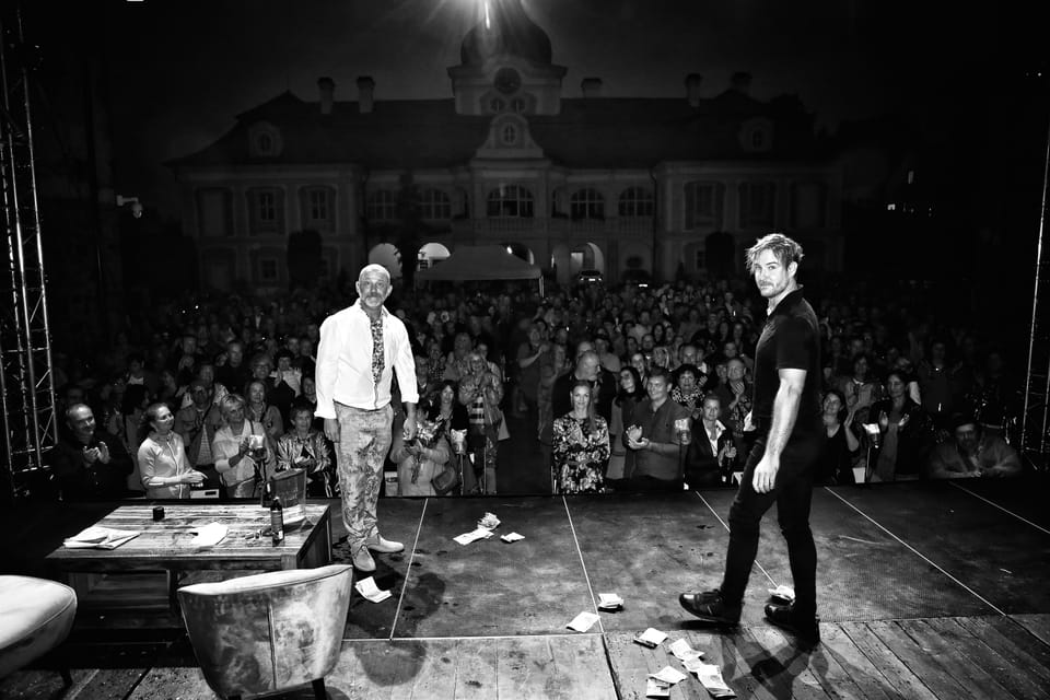 An open-air night performance in front of a chateau, two actors on stage and a full audience