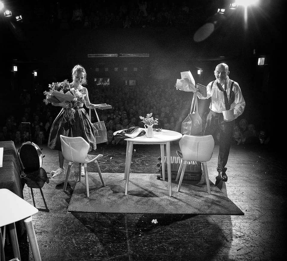 An open-air stage at night: an actress with a bouquet and a man with a double bass before a full square