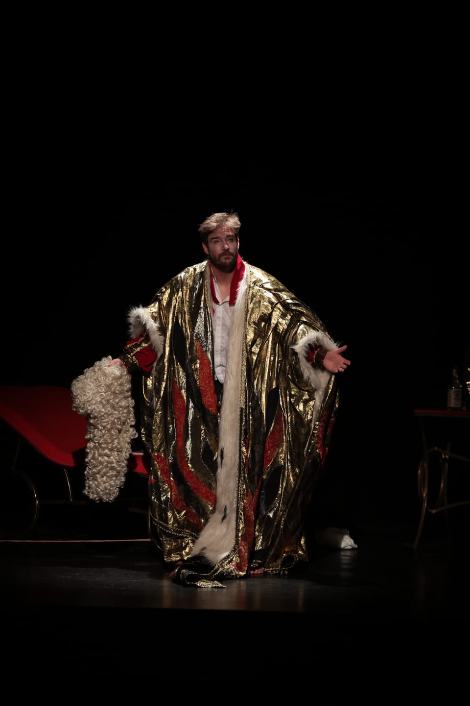 A figure in a heavy fur-trimmed cloak in the middle of a dark set