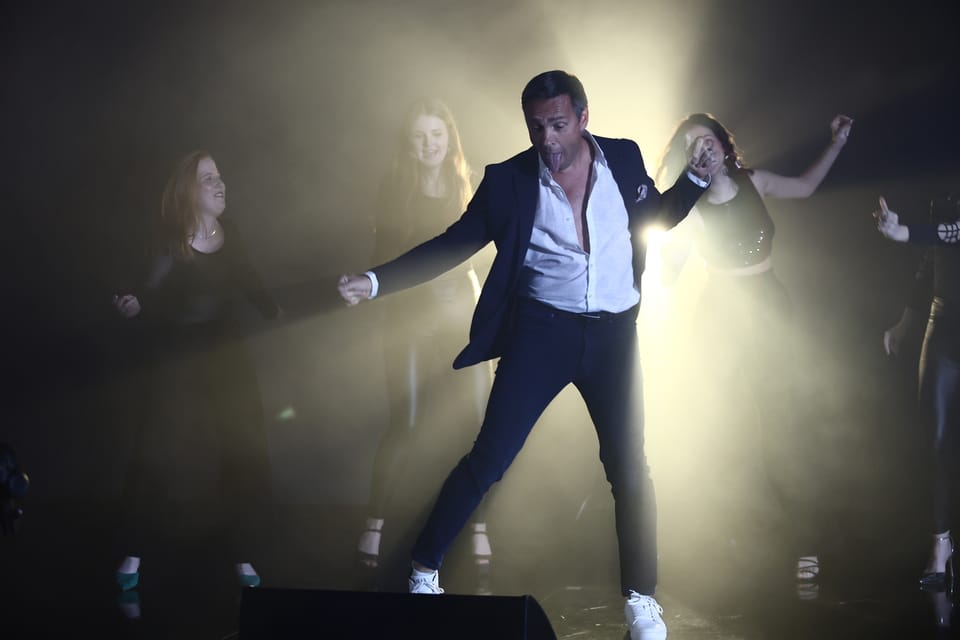 An actor in a white shirt stepping out of the backlight, other figures outlined around him