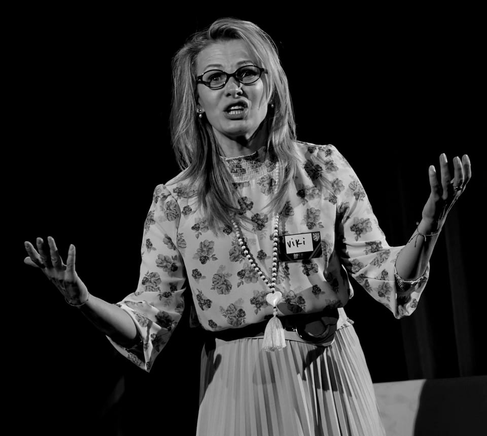 An actress in a floral blouse, hands thrown wide in mid-sentence