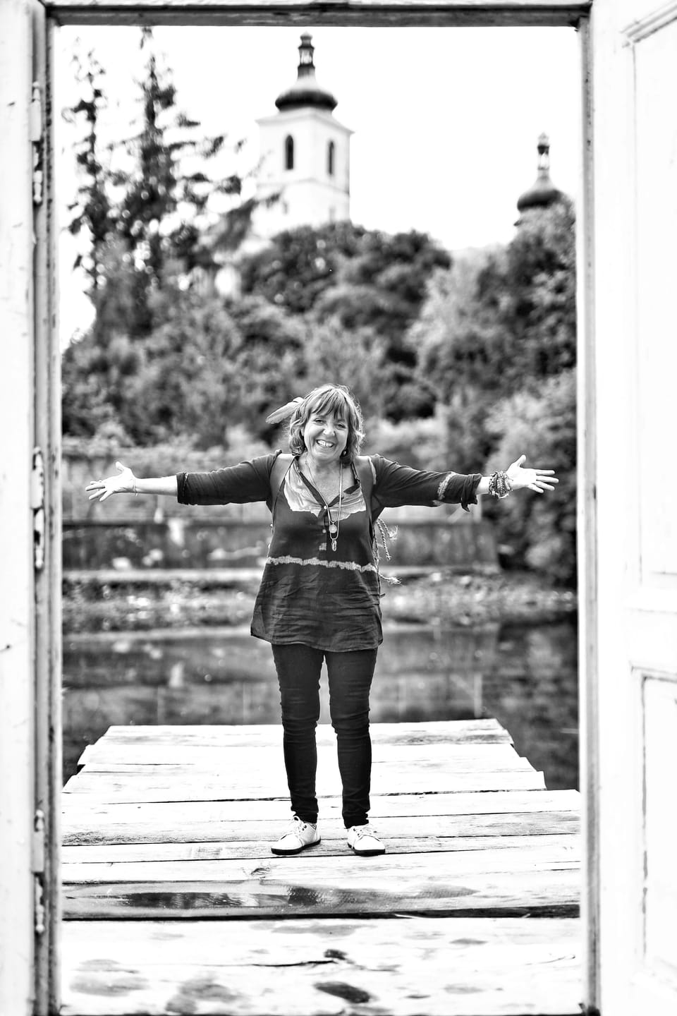A woman with arms spread standing in an open doorway, a church tower behind