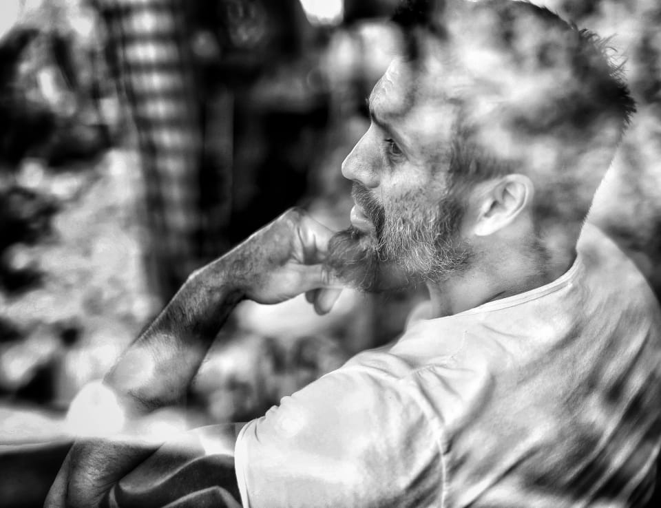 A bearded man in profile, hand at his face, the foreground blurred