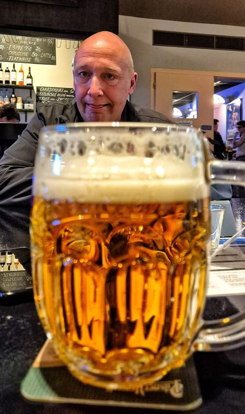 A foaming glass in the foreground, a blurred face and the noise of the bar behind