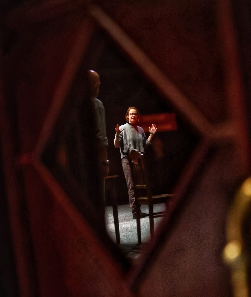 An actor on stage seen through a diamond-shaped cut in the scenery