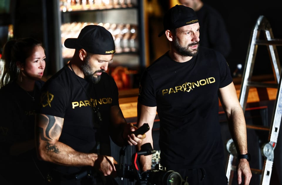A film crew at the camera, two men in team shirts checking the shot