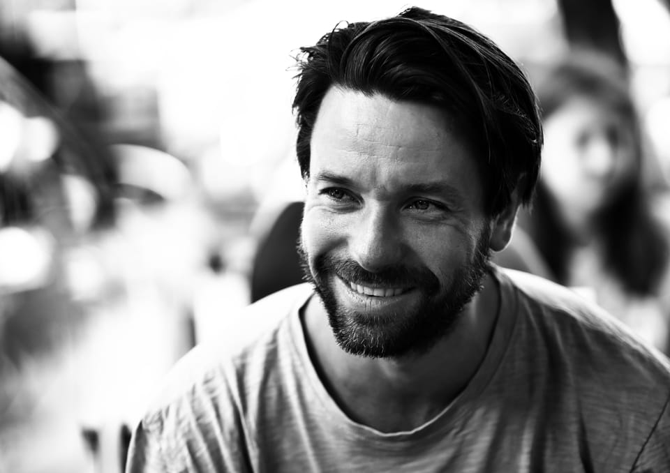 A smiling man in a grey T-shirt, the background dissolved into circles of light