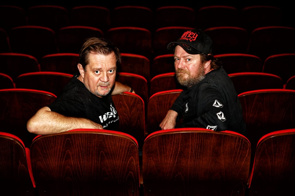 Two men sitting in an empty auditorium among the red seats