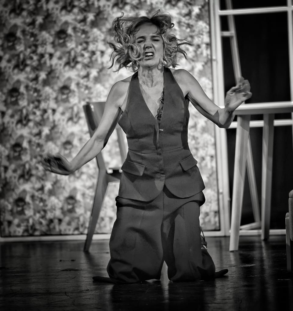 An actress on her knees, hair flying, hands thrown wide