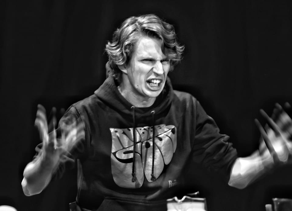 A young actor in a hoodie mid-shout, palms open before him