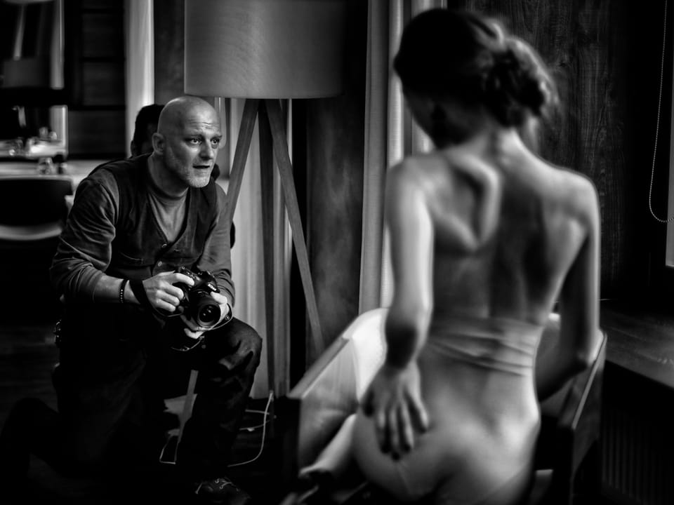 Behind the scenes of a shoot: a man with a camera and the model waiting in the studio