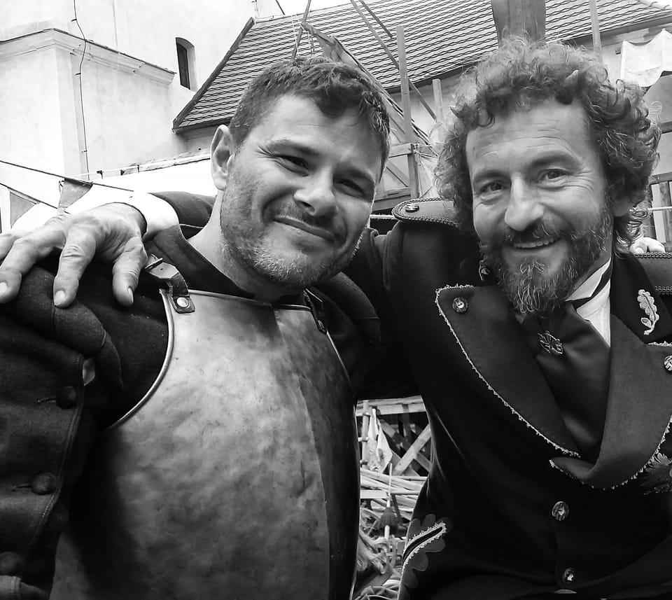 Two actors in armour and uniform, arms over shoulders, both laughing