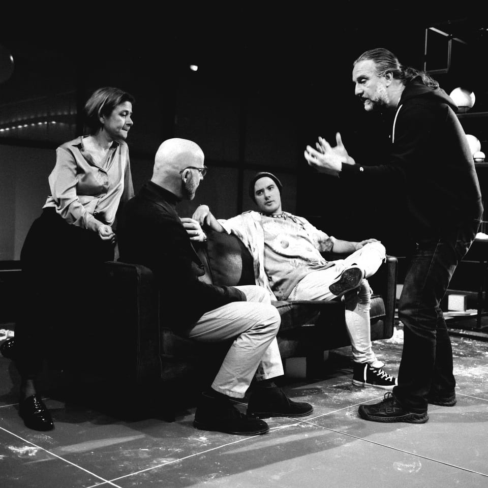 A rehearsal: five people around a sofa, one explaining with his hands