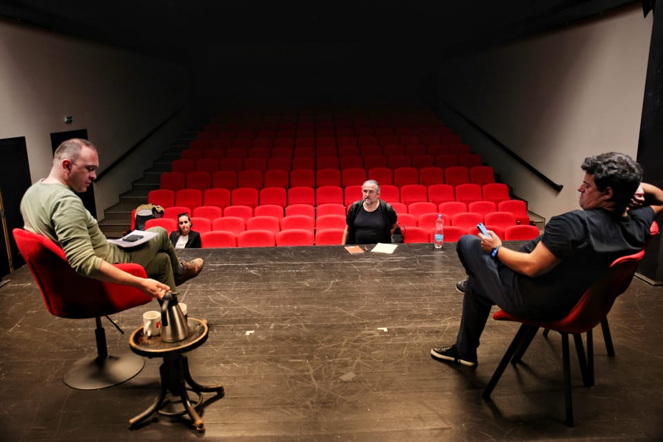 A rehearsal in an empty house, four people in armchairs facing rows of red seats