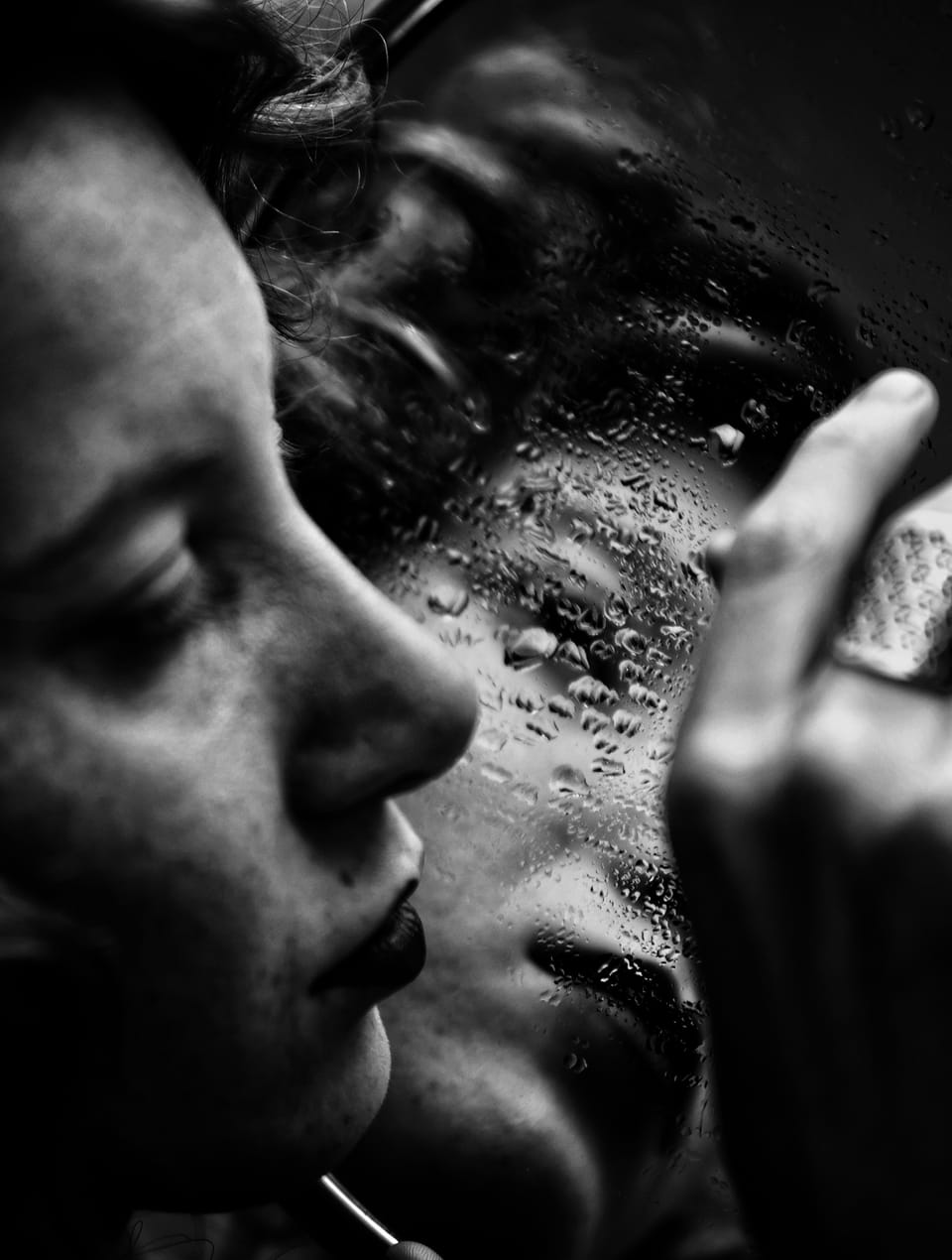 A woman's face behind fogged glass beaded with water, black and white