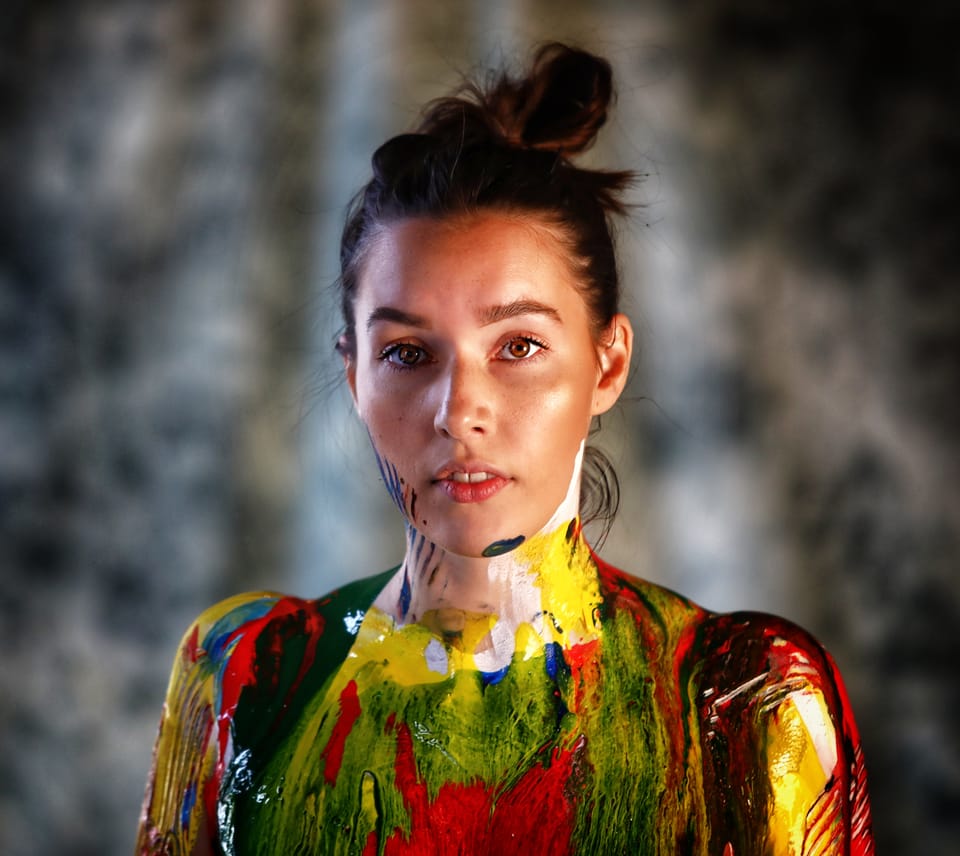 A portrait of a woman in paint-drenched clothing, the face left clean