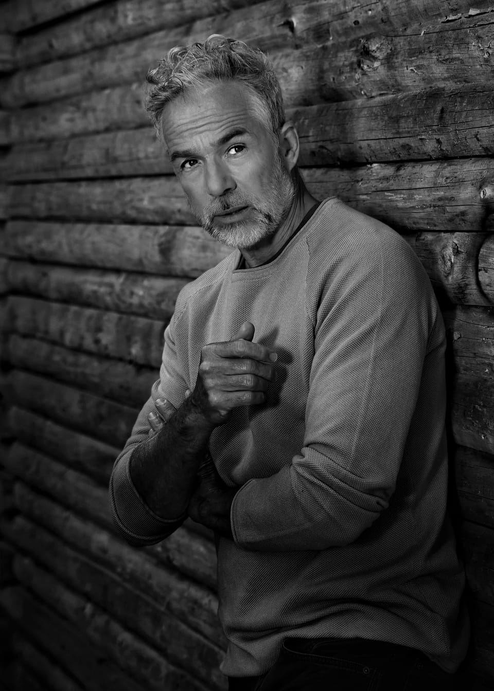 A grey-haired man in a boxer's guard against a wooden wall