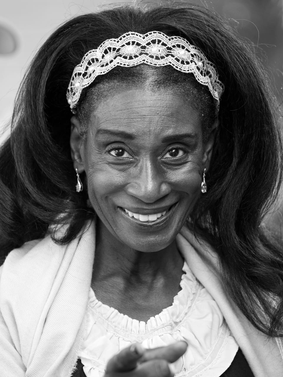 A woman in a lace headband and white blouse, the smile taking her whole face