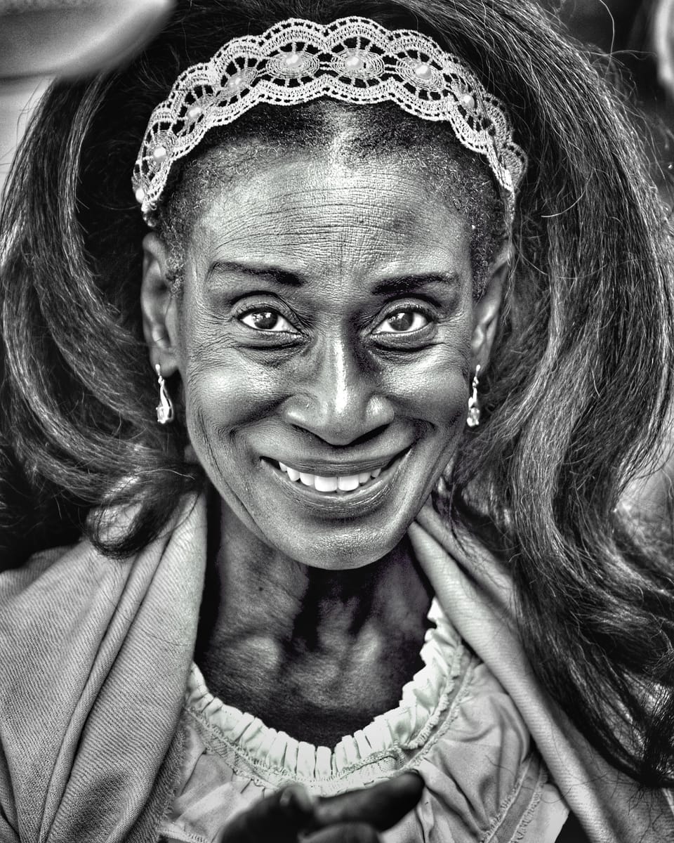 An older woman in a lace headband laughing openly into the lens