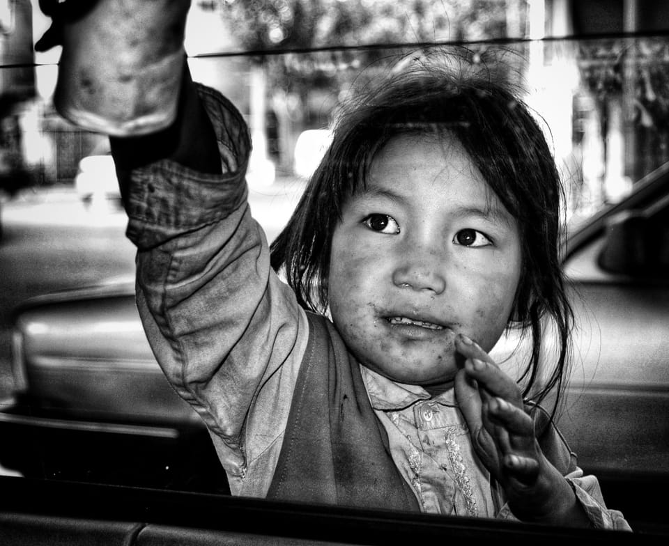 A child at a car window with an outstretched hand, the street reflected in the glass