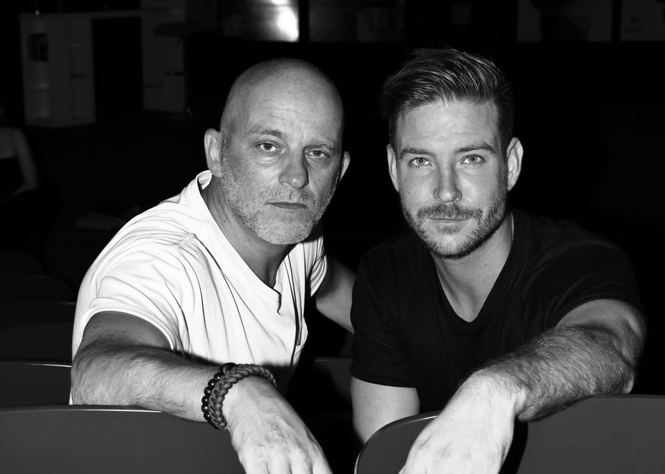 A black and white double portrait of two men leaning on theatre seats