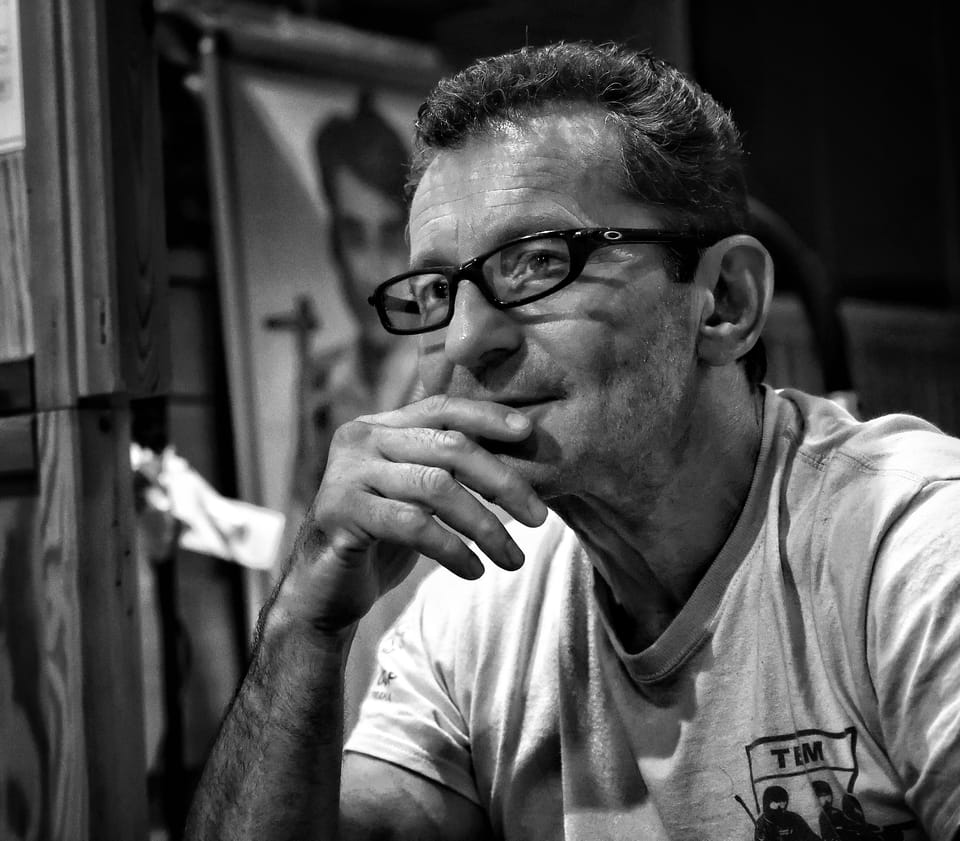A black and white portrait of a man in glasses, hand at his chin, looking away