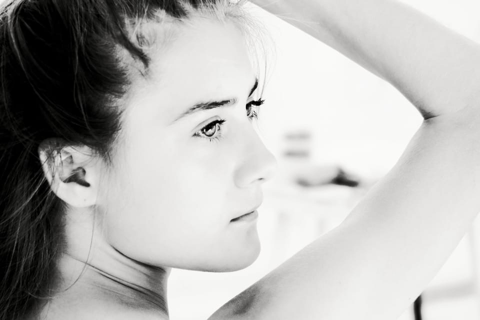 A young woman with one arm raised behind her head, looking aside into the light
