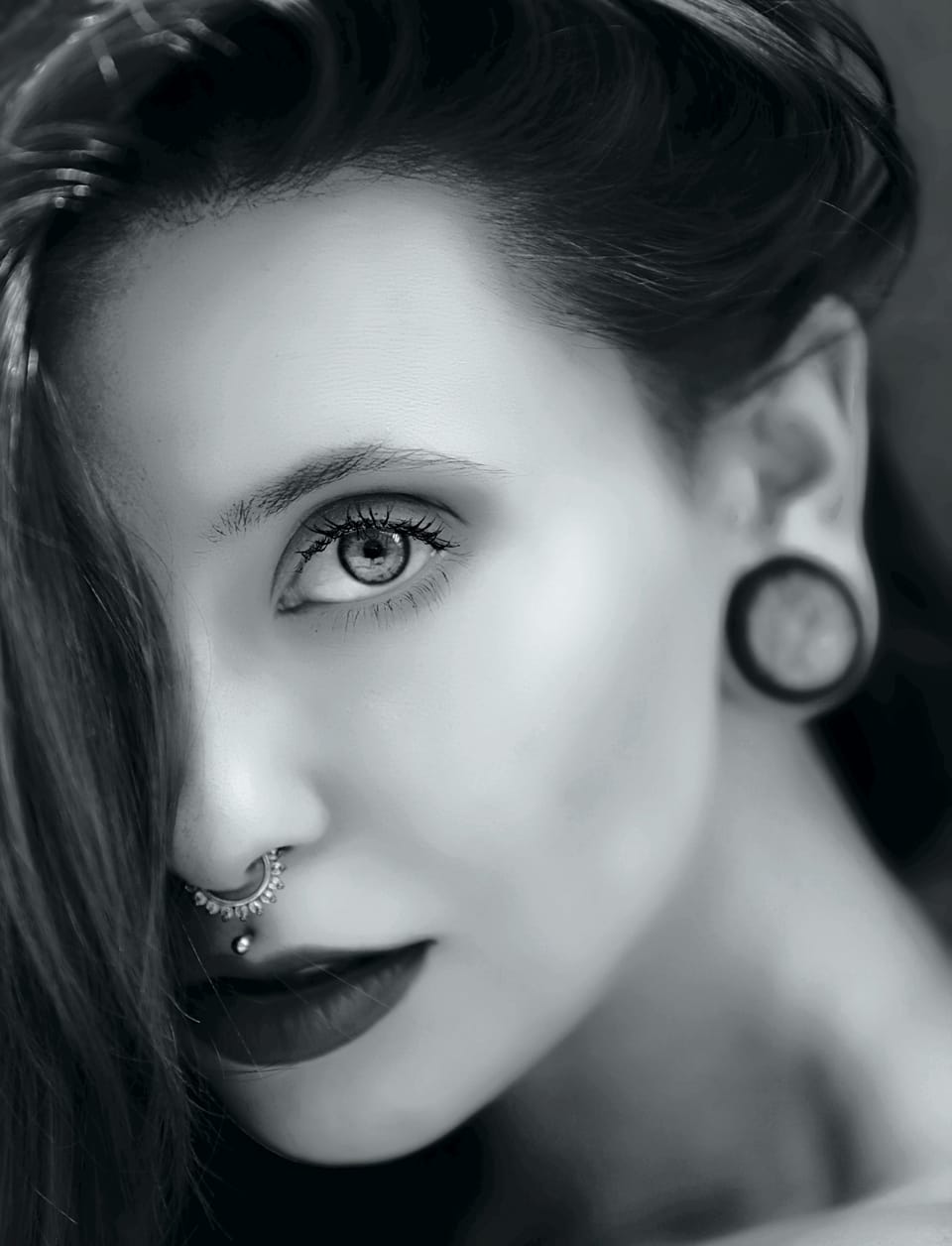 A close detail of a face with a nose ring and a stretched ear plug