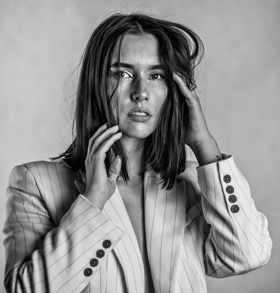 A woman in a pinstriped blazer, hands at her hair, clean studio light