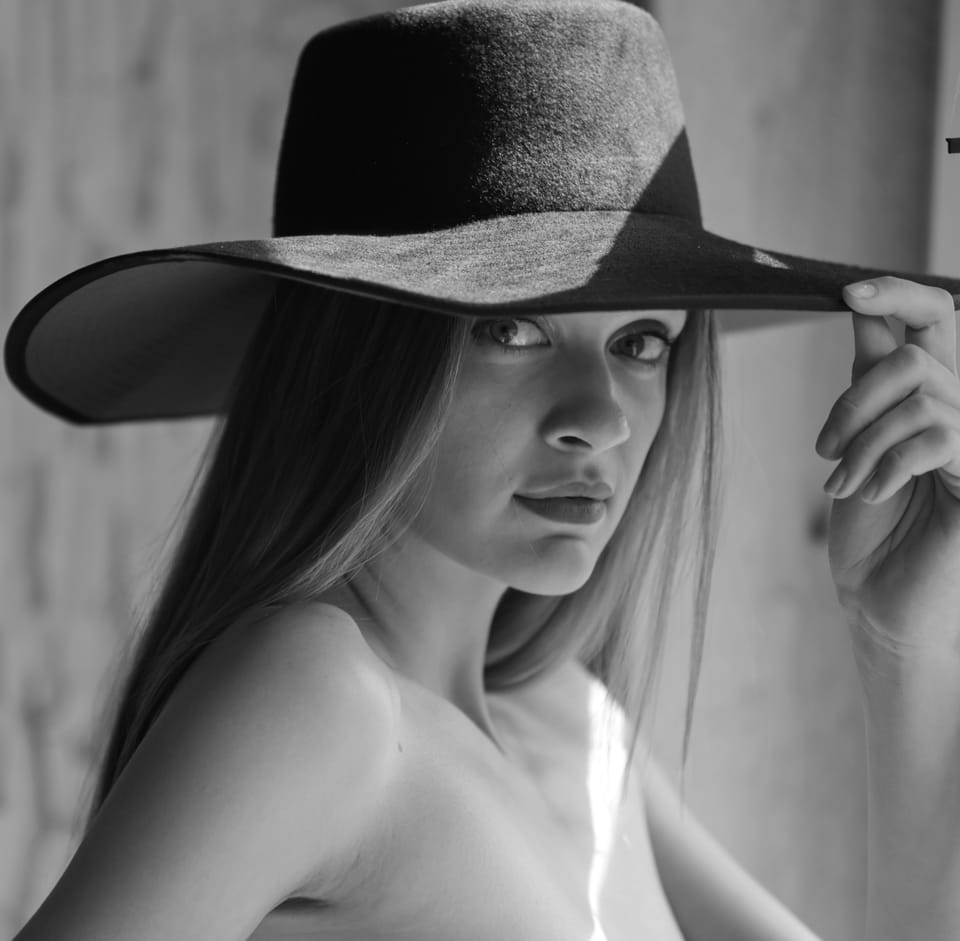 A woman in a wide-brimmed hat, fingers at the edge of the brim