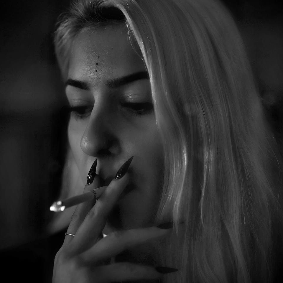 A lowered gaze and long nails at the cheek, the light falling from above