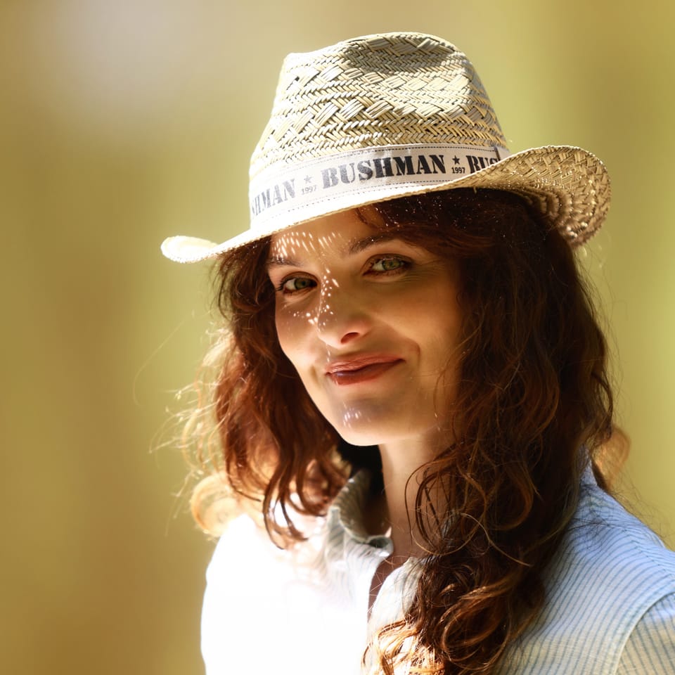 A red-haired woman in a straw hat smiling into warm backlight