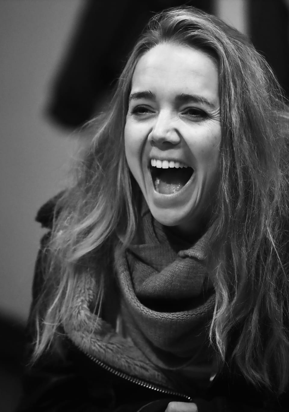 A black and white portrait of a young woman caught mid-laugh