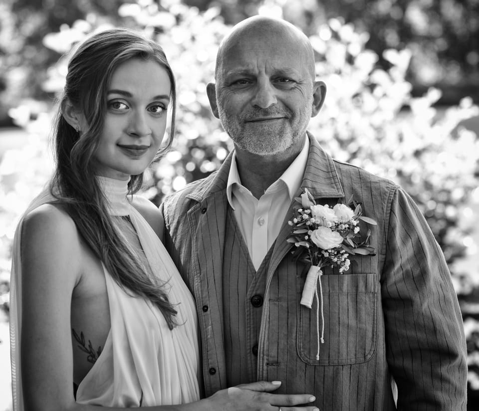 A couple dressed for the day, a flower in the man's lapel, blossom around them