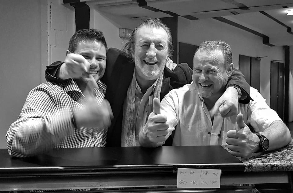 A black and white group portrait of three men with thumbs raised