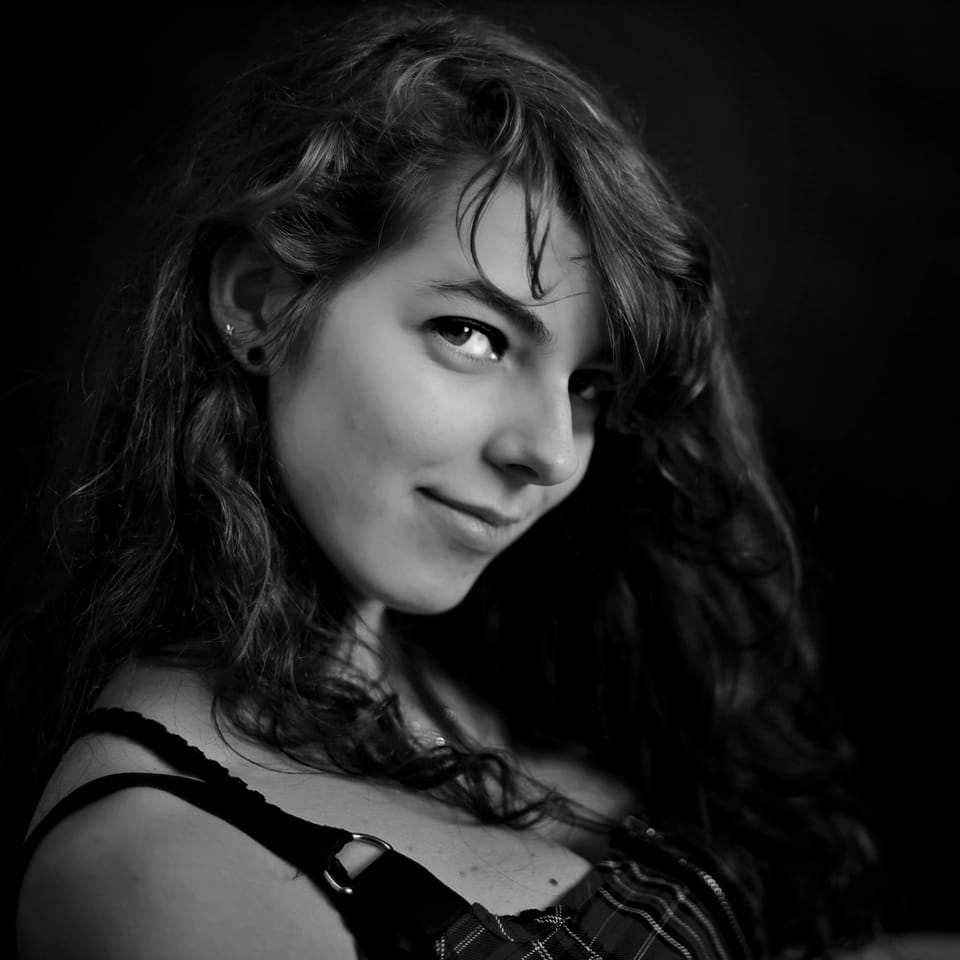 The smile of a young woman with curly hair against a dark ground