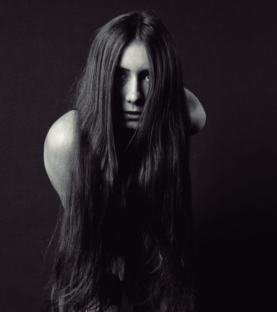 Hair fallen across the face, only shoulders and one eye coming out of the dark